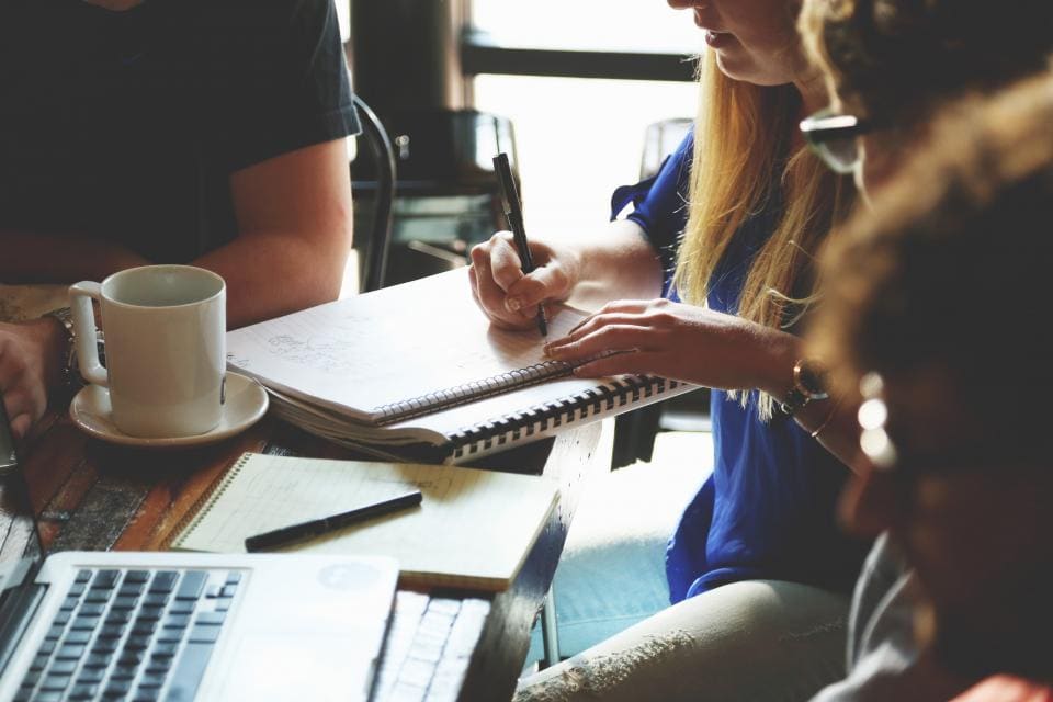 A team working around a shared table with notebooks and a laptop